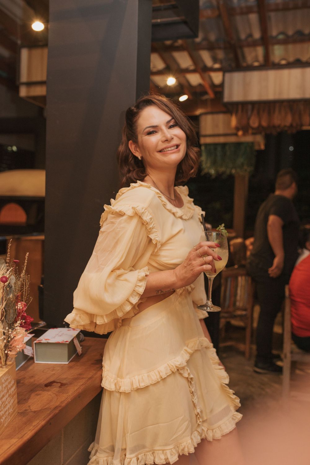 Person in a cream ruffled dress holds a champagne glass at an indoor celebration.