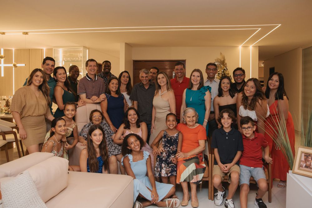 Large group photo of friends and family gathered in a modern living room for a celebration.
