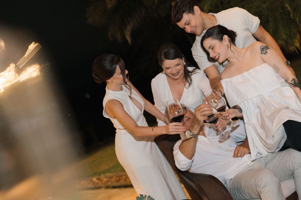 Group shares drinks and laughter while dressed in coordinated white outfits.