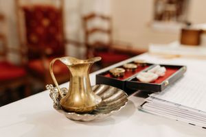 Golden brass pitcher and shell-shaped dish on white altar table with liturgical items in background.