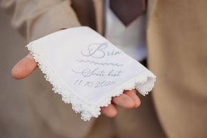 Groom holding a personalized white lace handkerchief with embroidered wedding date script.