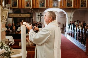 Catholic priest in white vestments lighting a candle on the altar during a church ceremony.