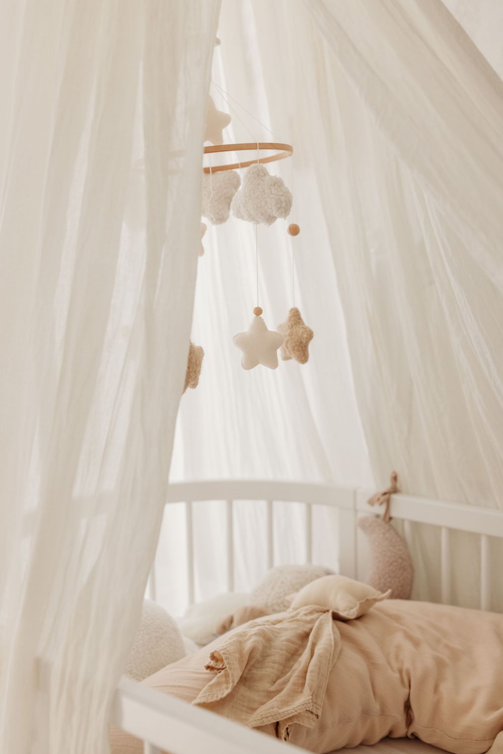 Cozy white baby crib with canopy, soft beige bedding, and hanging mobile with stars and clouds.
