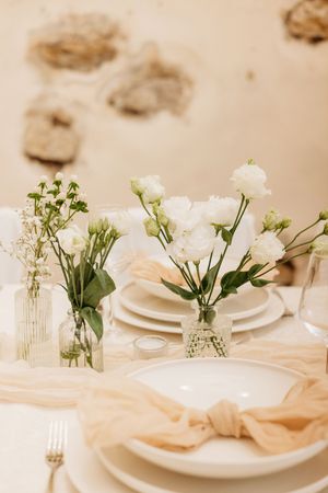 Elegant wedding table setting with white roses, baby's breath, cream napkins, and white plates in a soft neutral decor.