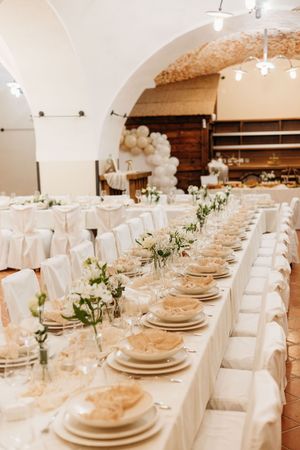 Elegant white wedding reception banquet hall with long decorated tables and floral centerpieces.