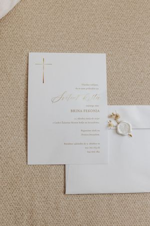 Elegant gold cross baptism invitation with cursive script and wax seal envelope on neutral linen background.