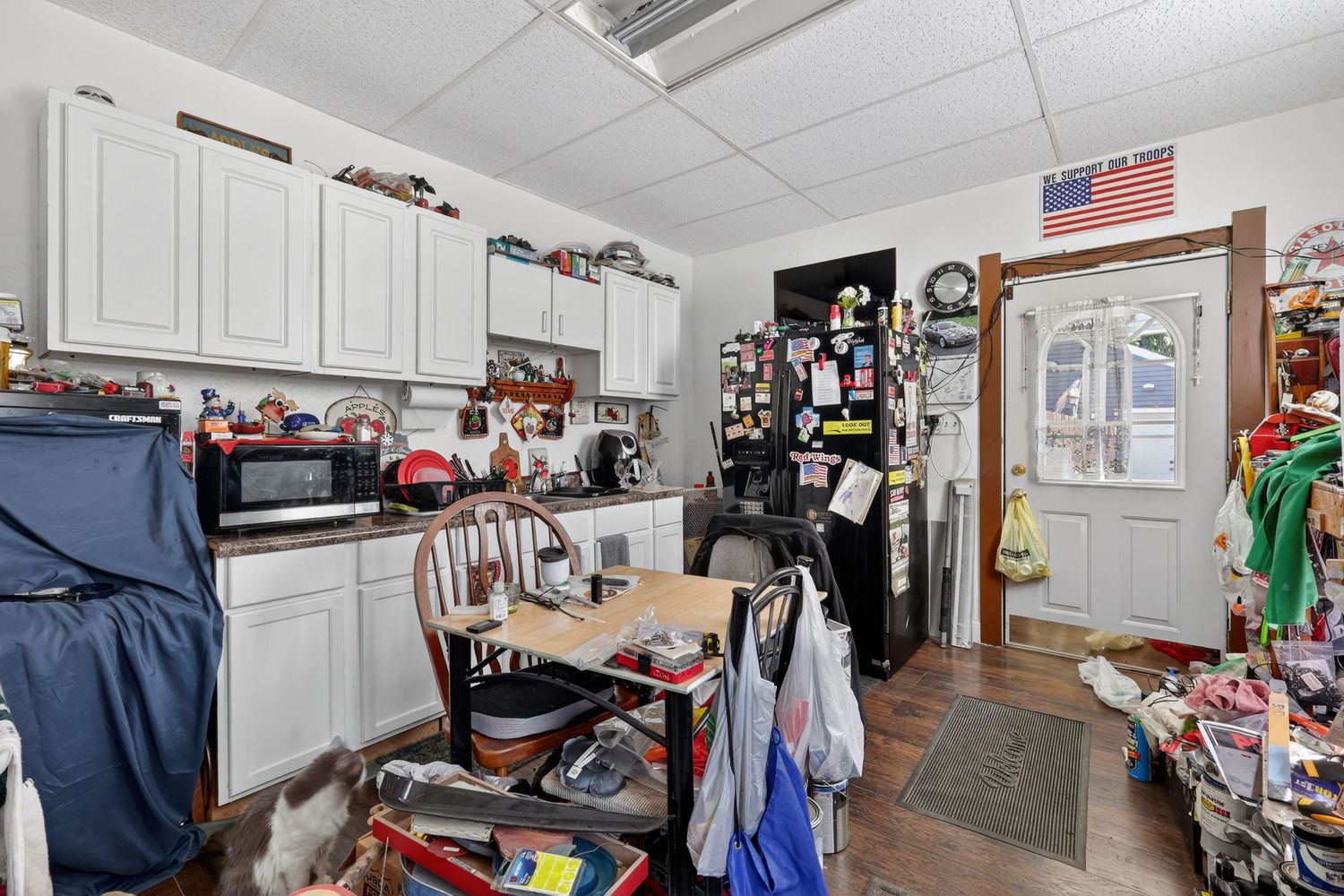 Small kitchen featuring white cabinetry, drop ceiling, hardwood floors, American flag decor, and door leading outside.