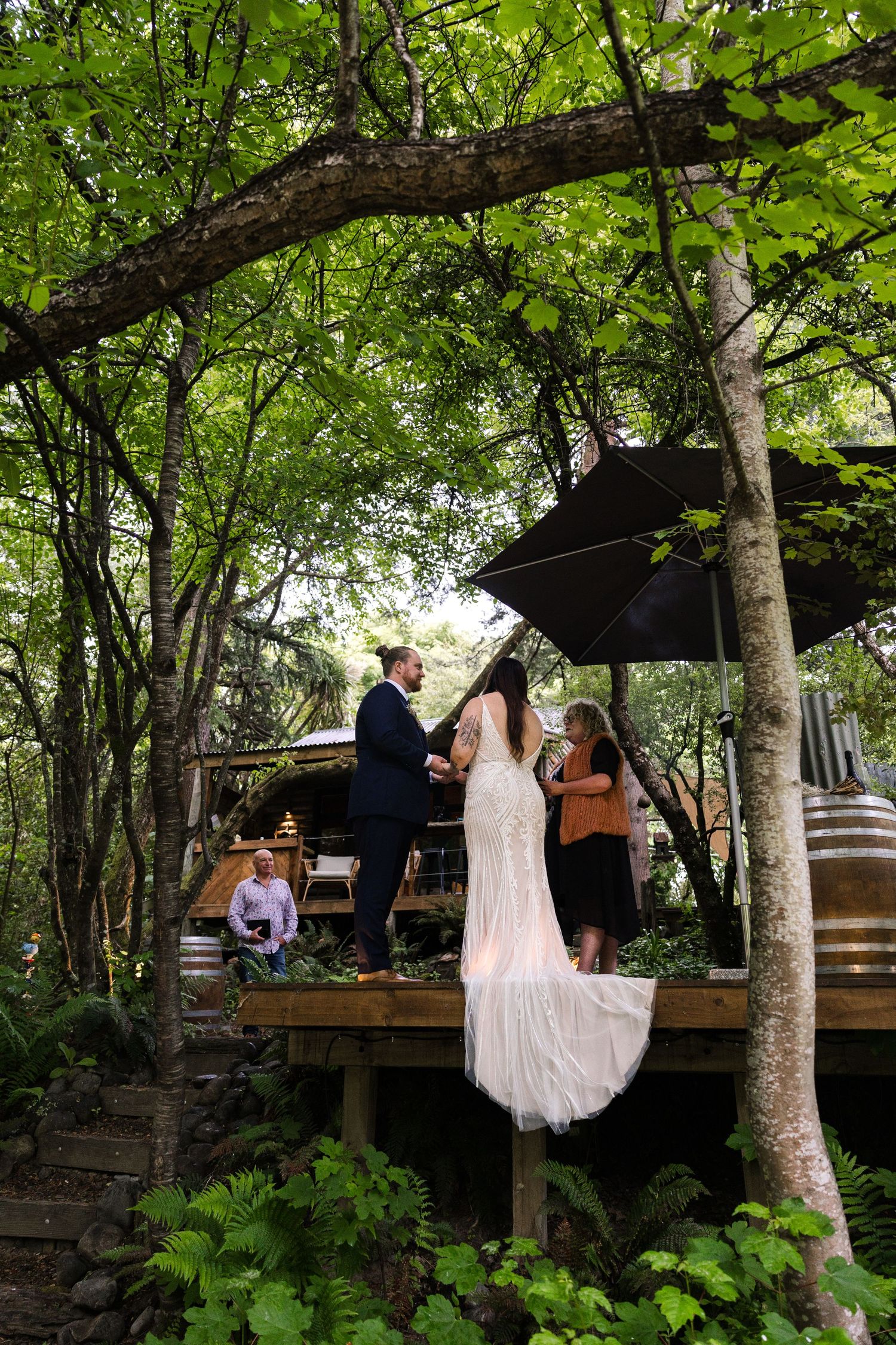 bride in white lace gown stands with groom in sunlit outdoor wedding ceremony at little rock elopements in new zealand.