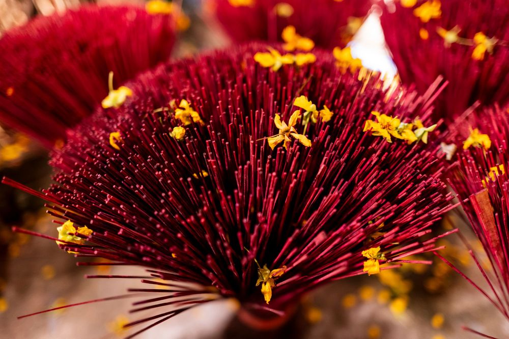 Vibrant red incense sticks bundled together with yellow flowers in a traditional Asian temple offering.