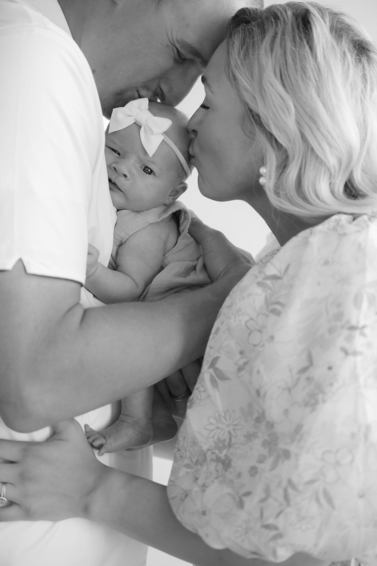 baby laying on dad's chest while both parents kiss baby on the head during in studio lifestyle newborn portraits in stillwater, mn