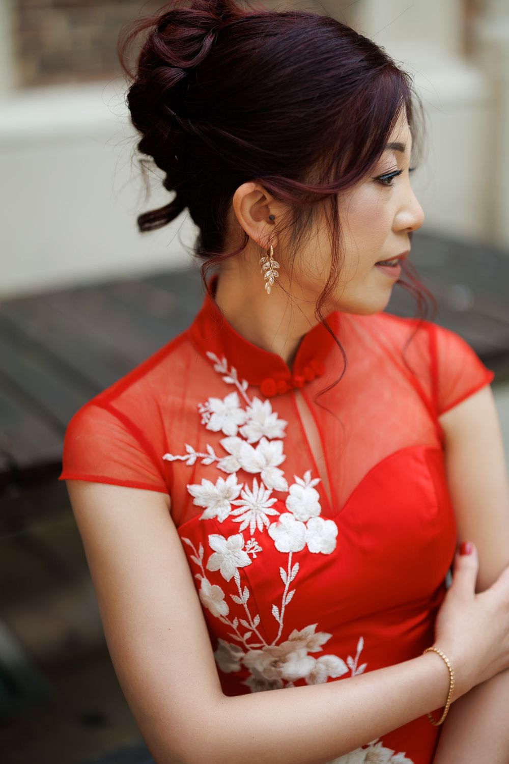 Young woman in red floral cheongsam qipao dress with white embroidery, elegant updo hairstyle and drop earrings.