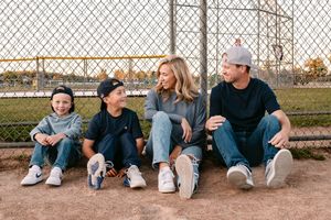 Family of four sitting together on a baseball field bleachers, smiling and chatting in casual sporty outfits.