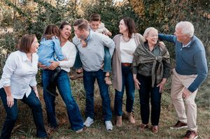 Multi-generational family laughing together outdoors in a casual photo session among green trees.