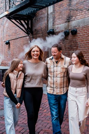 A happy family of four walks together on a brick street in an urban setting, smiling and enjoying time together.