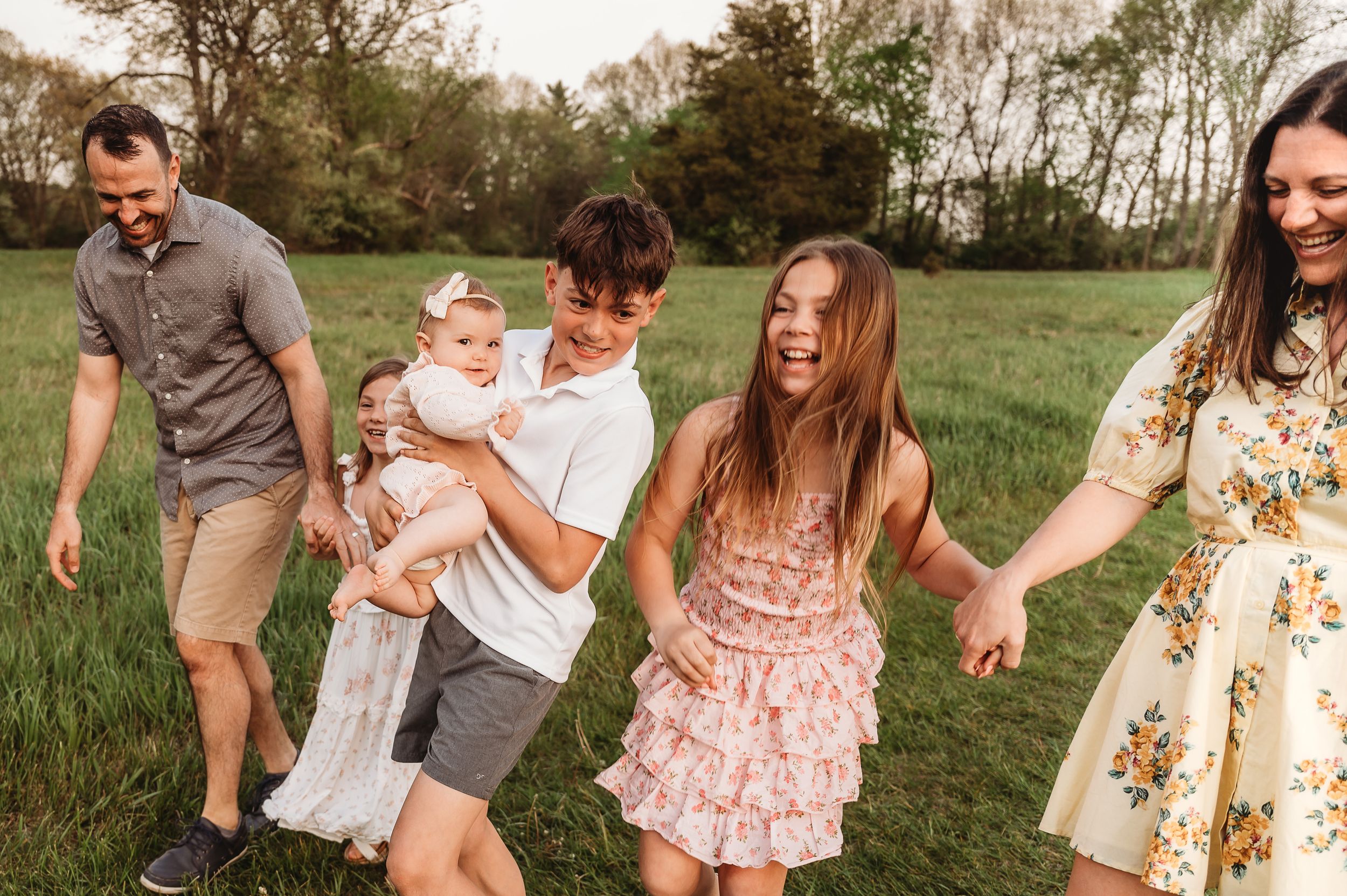 Happy family walking outdoors in a green field, laughing and holding hands during a candid photo session.
