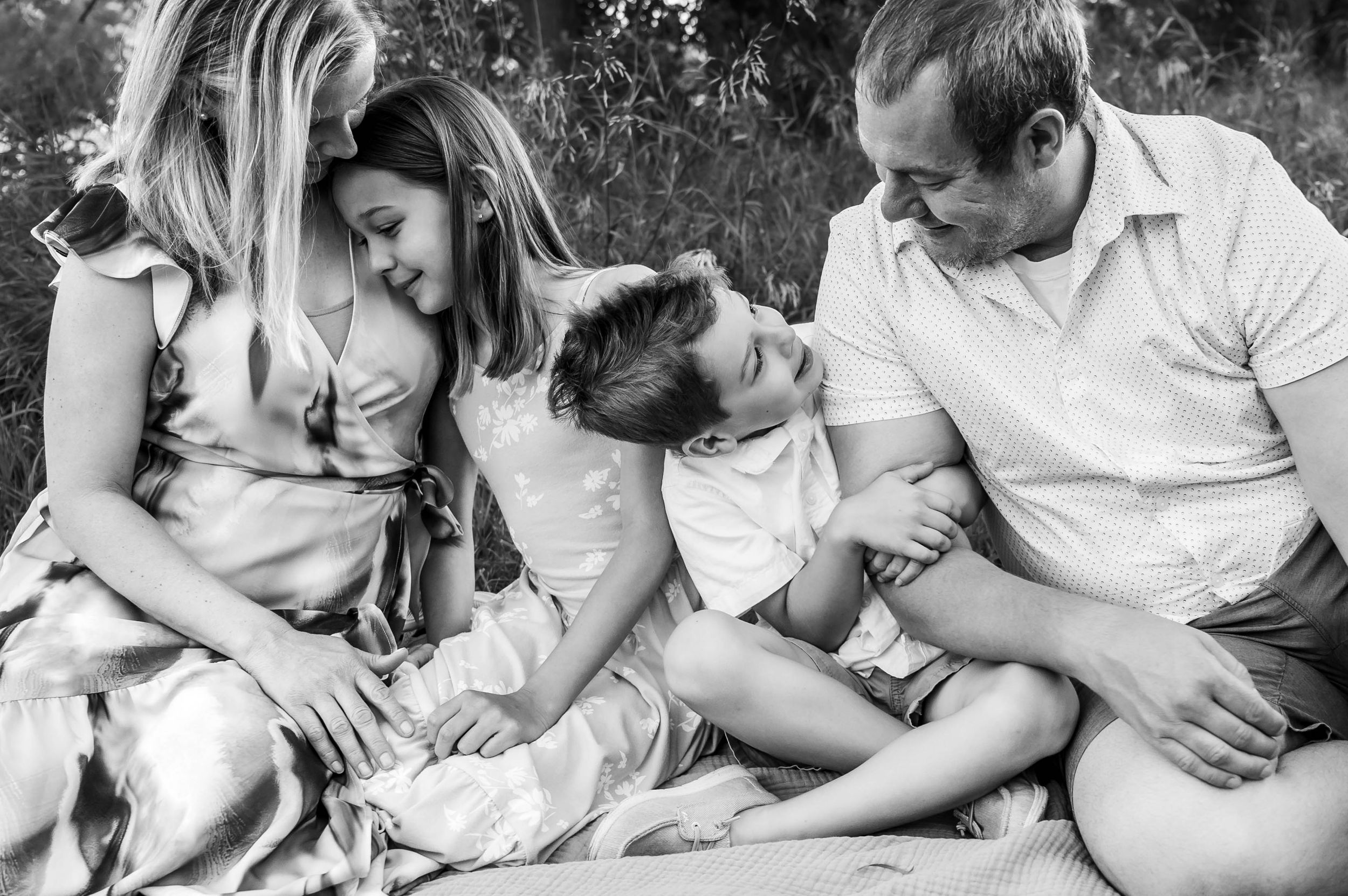 A black and white photo of a family of four sitting closely together on a blanket outdoors.