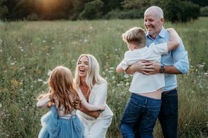 A joyful family laughs and embraces in a blooming meadow during a beautiful golden hour sunset.