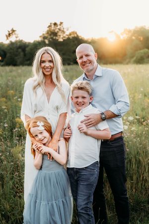 A smiling family of four poses together in a wildflower field during a warm golden sunset.