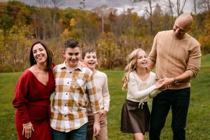 Happy family of five laughing together outdoors in autumn park with colorful fall foliage background.