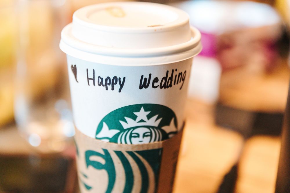Starbucks cup with Happy Wedding written in marker on white paper cup with green mermaid logo.