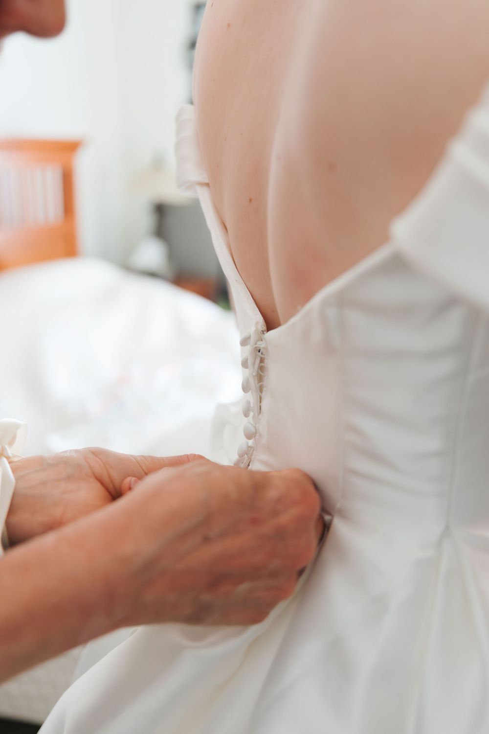 mother buttoning the back of a white wedding dress on a bride, with small pearl buttons running down the gown. Edmonton wedding photos