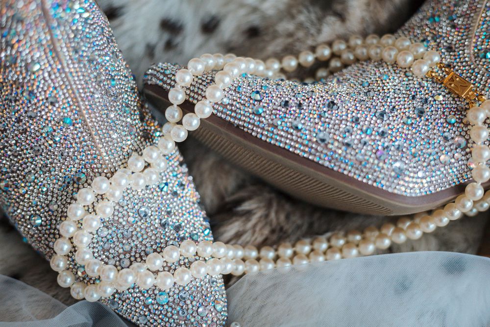 Crystal rhinestone embellished shoes adorned with pearl necklaces on a fur background.