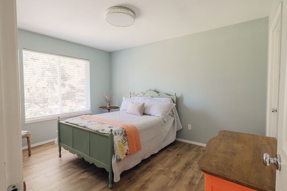 Bright bedroom with green metal bed frame, peach accent, and light sage green walls.