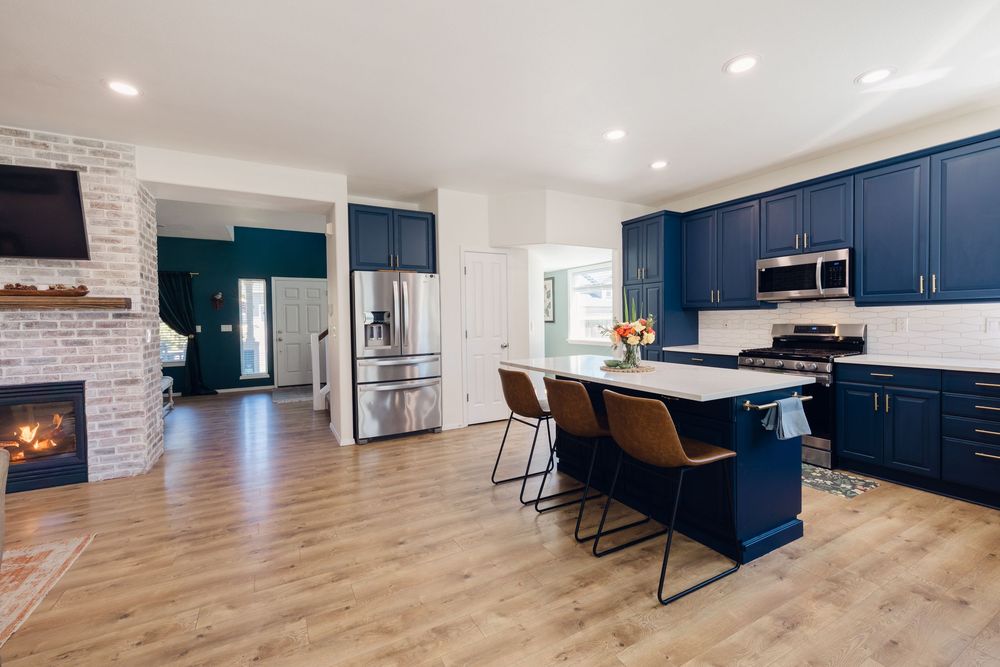 Modern kitchen with navy blue cabinets, white quartz island, bar stools, hardwood floors, and brick fireplace.
