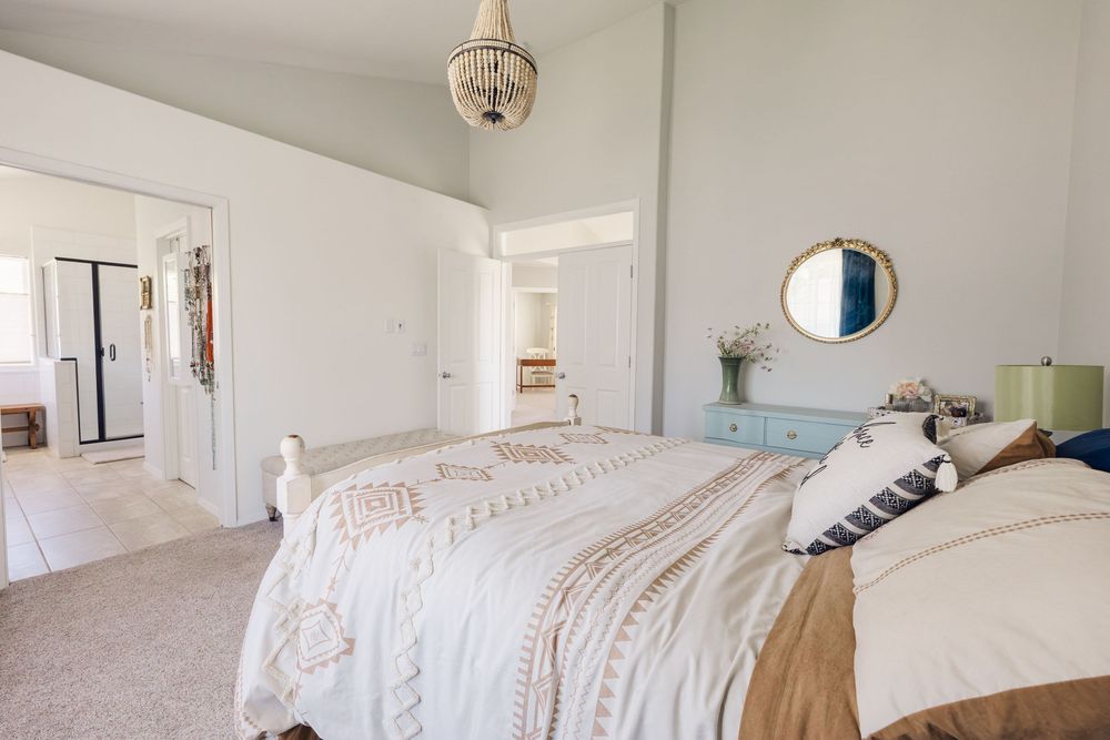 Bright master bedroom with high ceilings, beige carpet, chandelier, and light blue dresser with mirror.