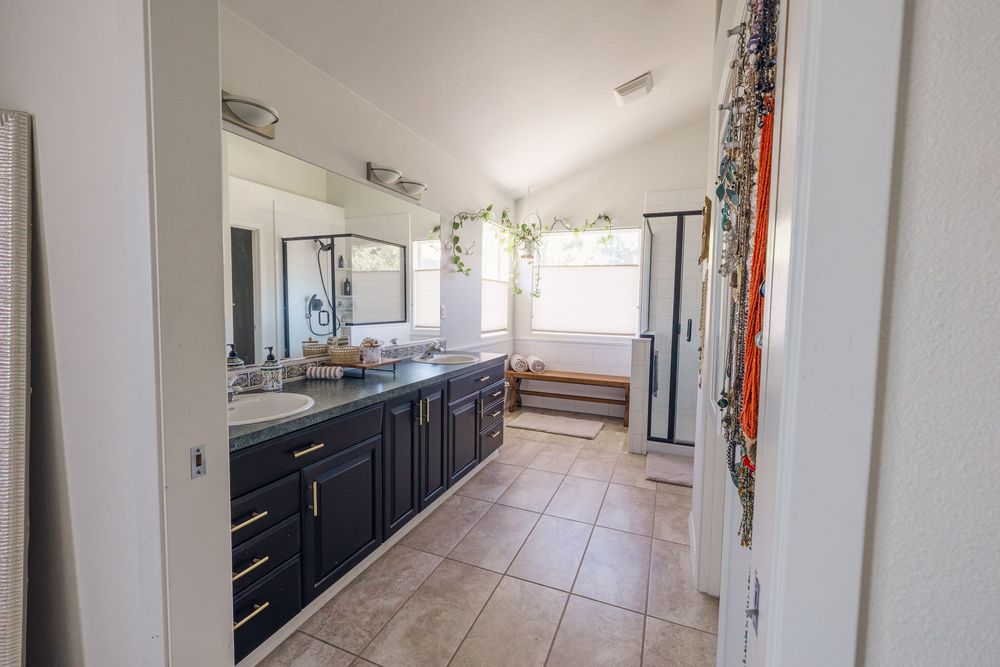 Spacious bathroom with dark navy cabinets, dual sinks, large mirror, and tile flooring.