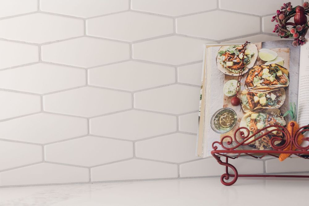White hexagon kitchen backsplash tiles with a cookbook on a decorative red metal stand.