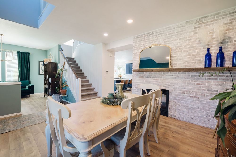 Bright dining room with wooden table, white brick fireplace, and open staircase in modern home.