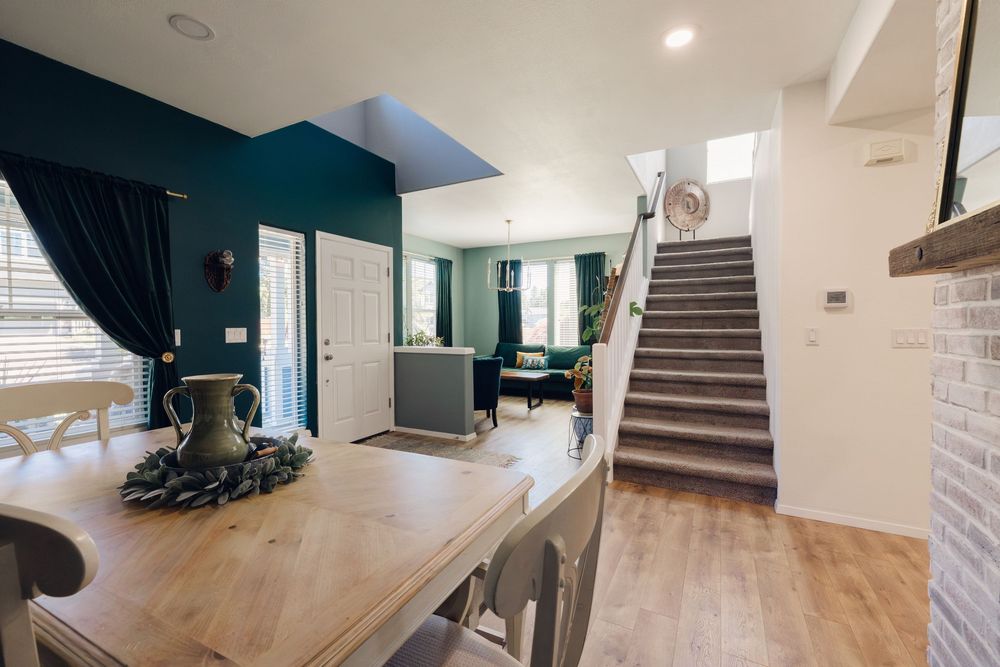 Open-concept living space featuring teal accent wall, wood staircase, and natural light-filled interior.