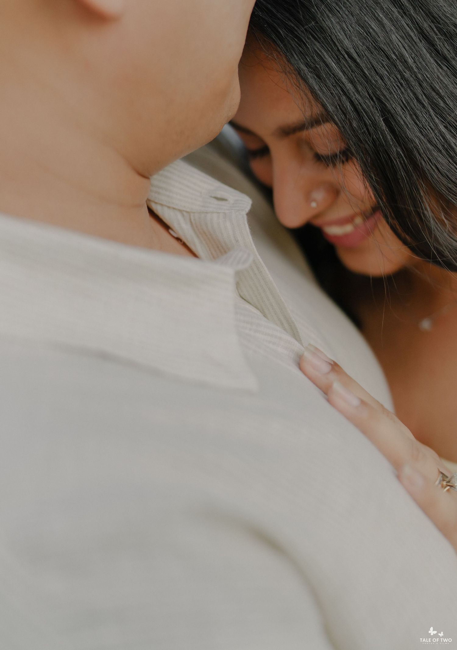 A couple shares an intimate moment, with a smiling woman leaning close to a man in a cream ribbed sweater.