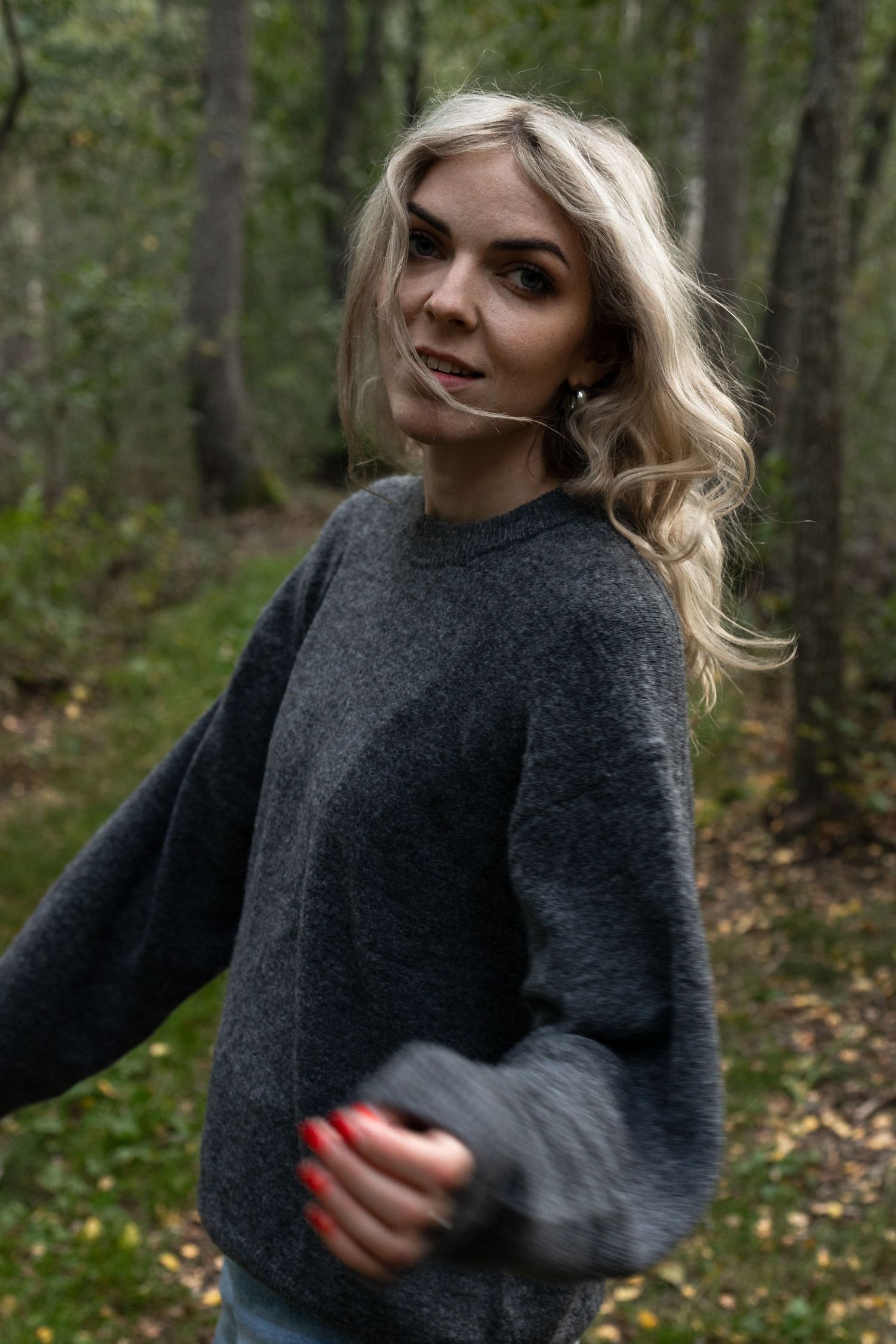 Kvinna i grå tröja står i en skog med höstfärger och mjukt ljus