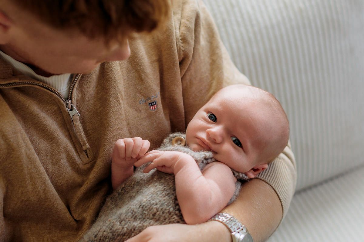 Nybakt far som holder sin nyfødte sønn i armene og kikker ned på ham. Babyen ser i kameraet.