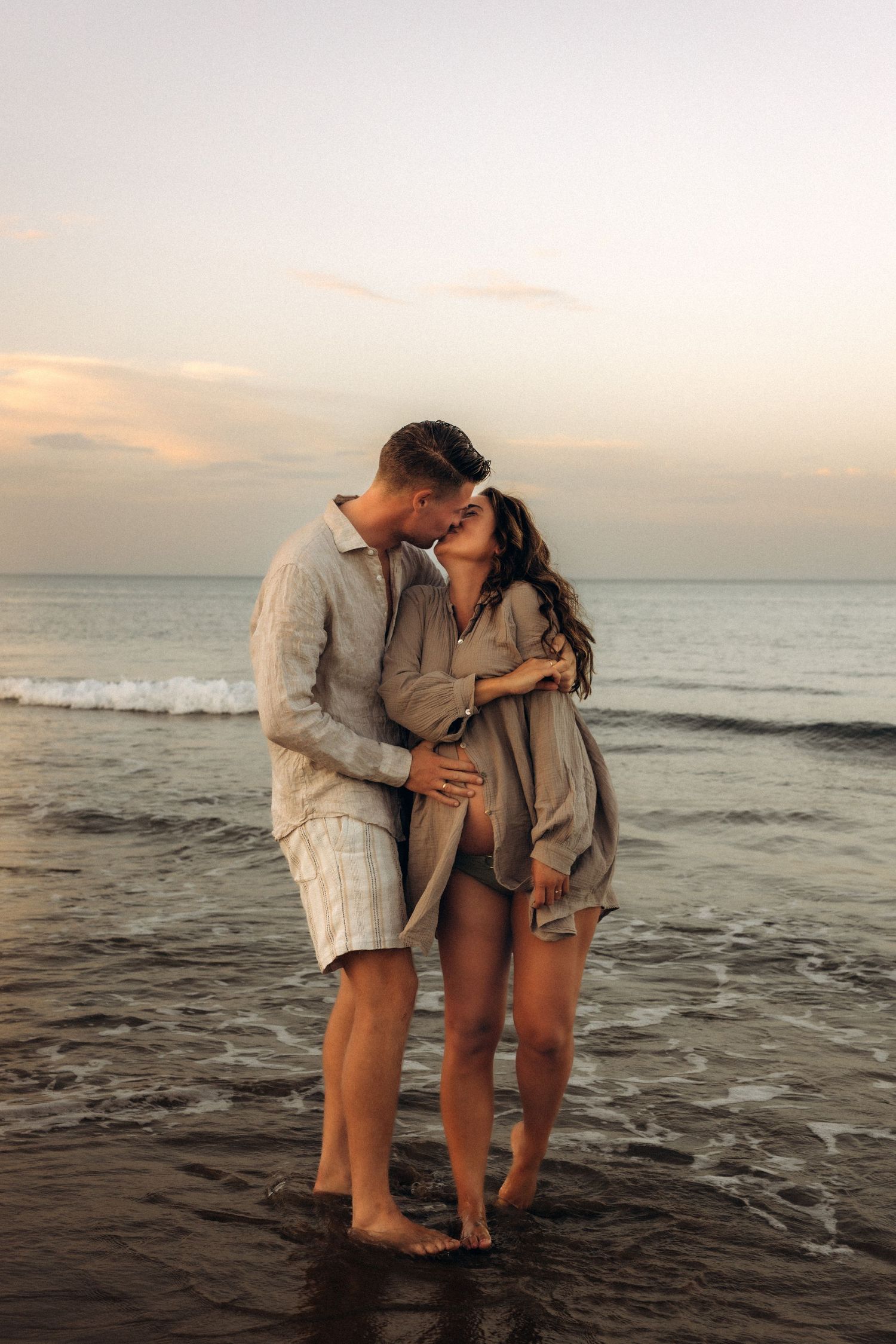A couple shares an intimate moment in Denia on the beach at sunset, standing barefoot . Denia maternity photographer