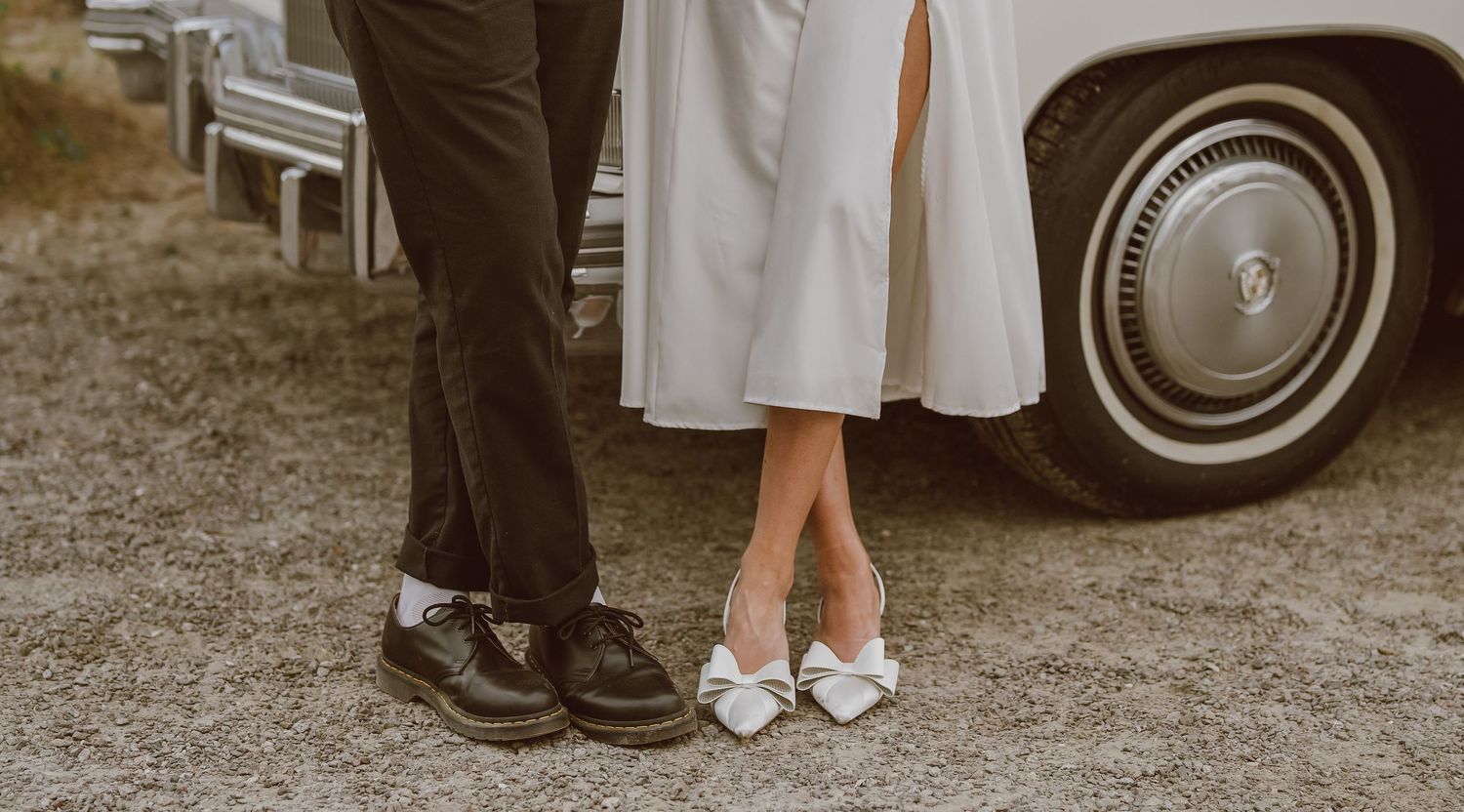 Close-up view of formal shoes and dress hem next to a vintage car wheel.