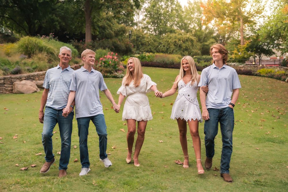 Family holding hands while walking together on grassy lawn in coordinated outfits.