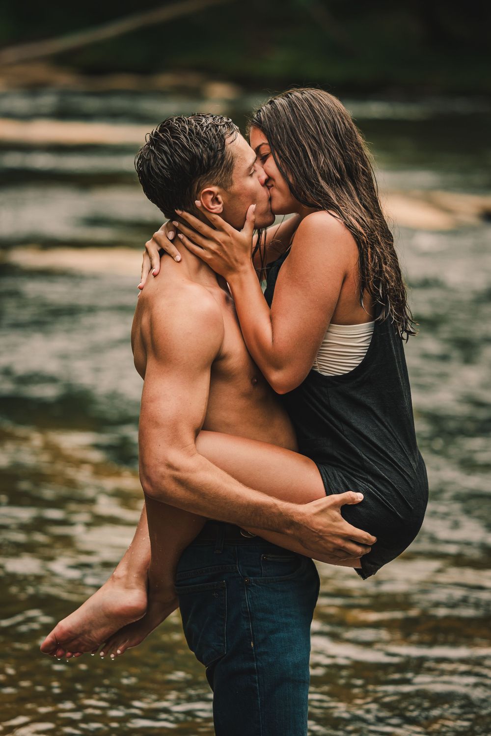 A passionate embrace captured in a river with lush forest backdrop and golden hour lighting.