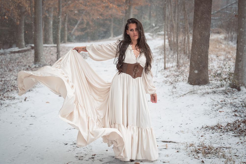 A figure in a flowing white dress twirls gracefully in a snowy winter forest setting.