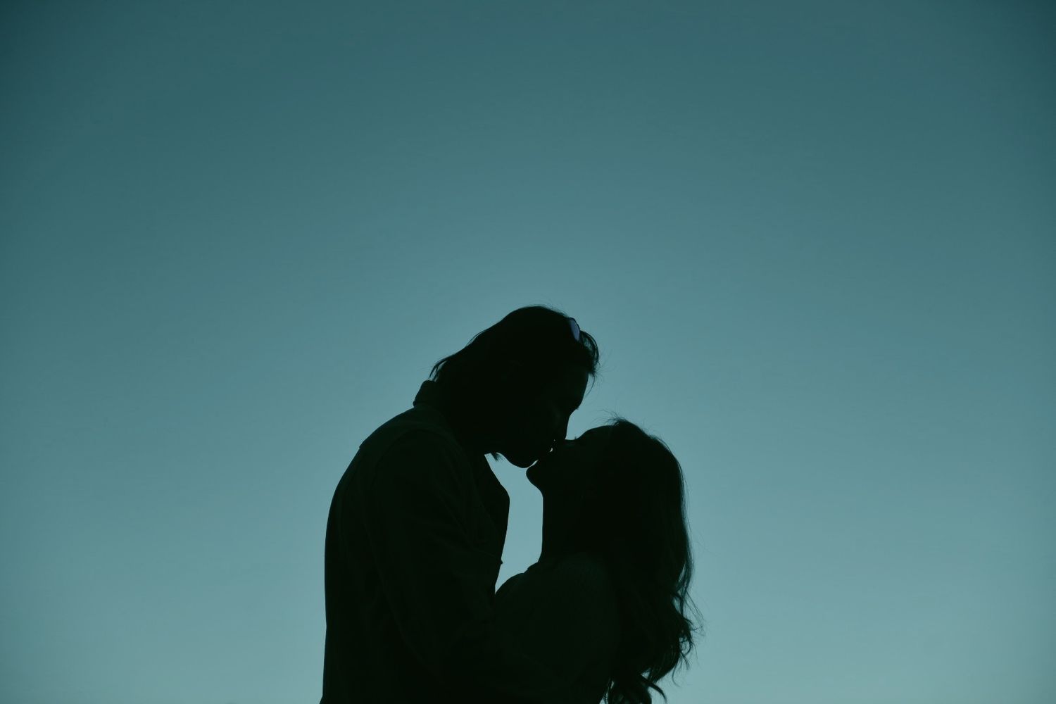 A silhouette portrait of a couple embracing and kissing.