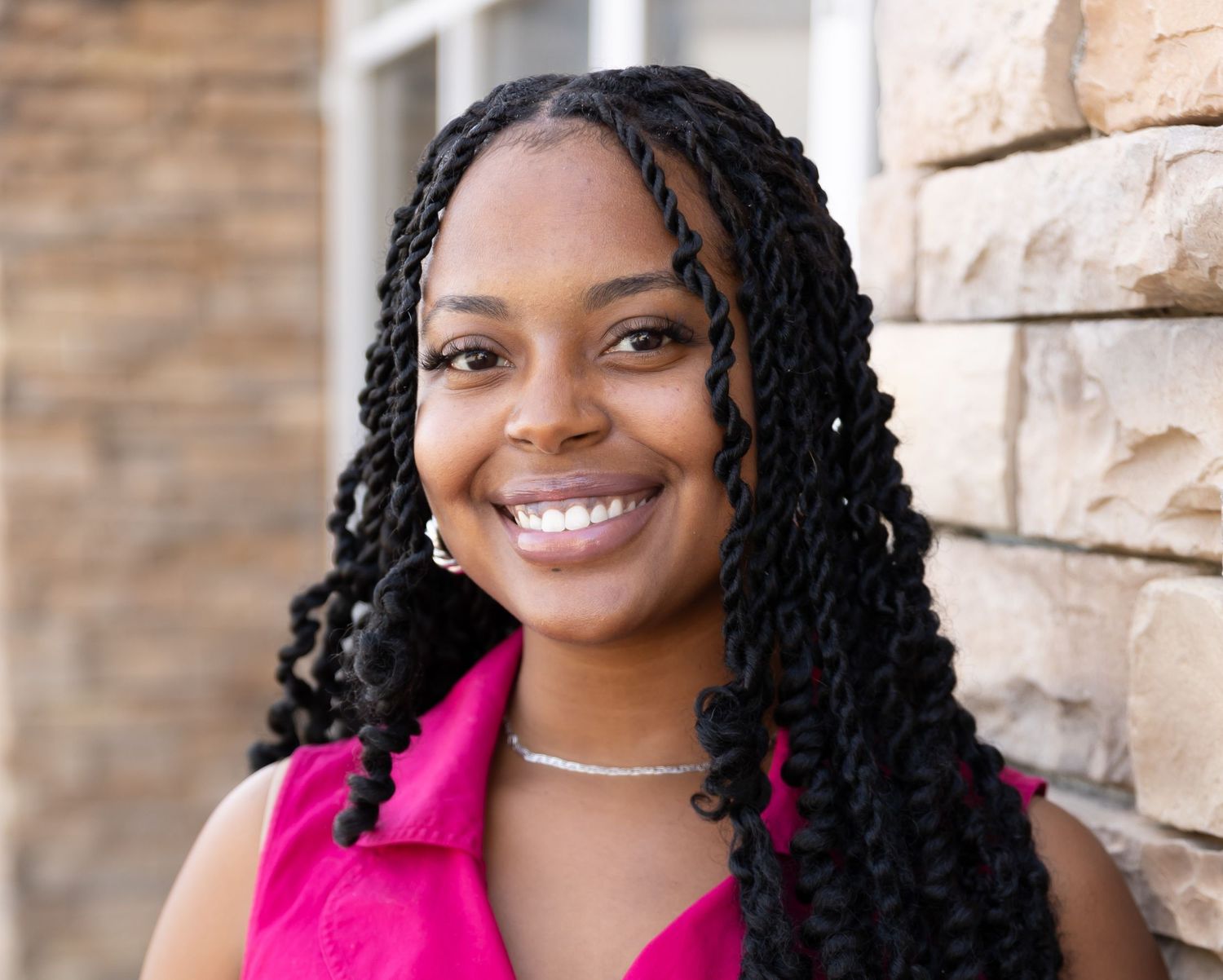 Professional headshot series in front of stone wall featuring bright pink attire.