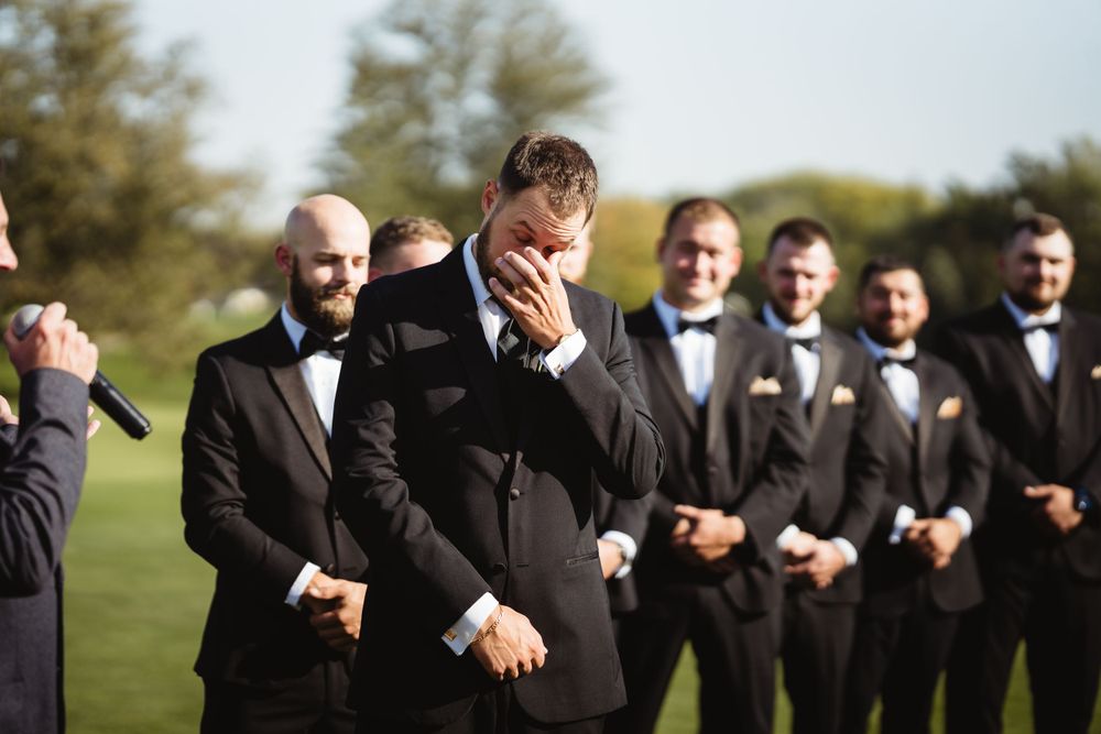 An emotional moment during a wedding ceremony with groomsmen in black suits.