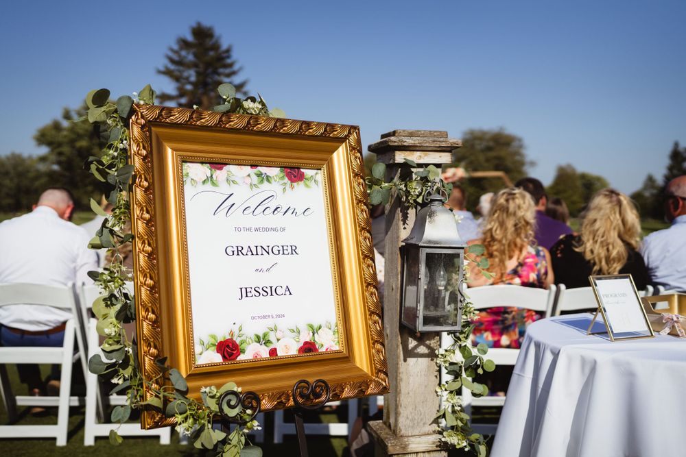 An ornate gold frame with wedding details sits among outdoor reception tables.