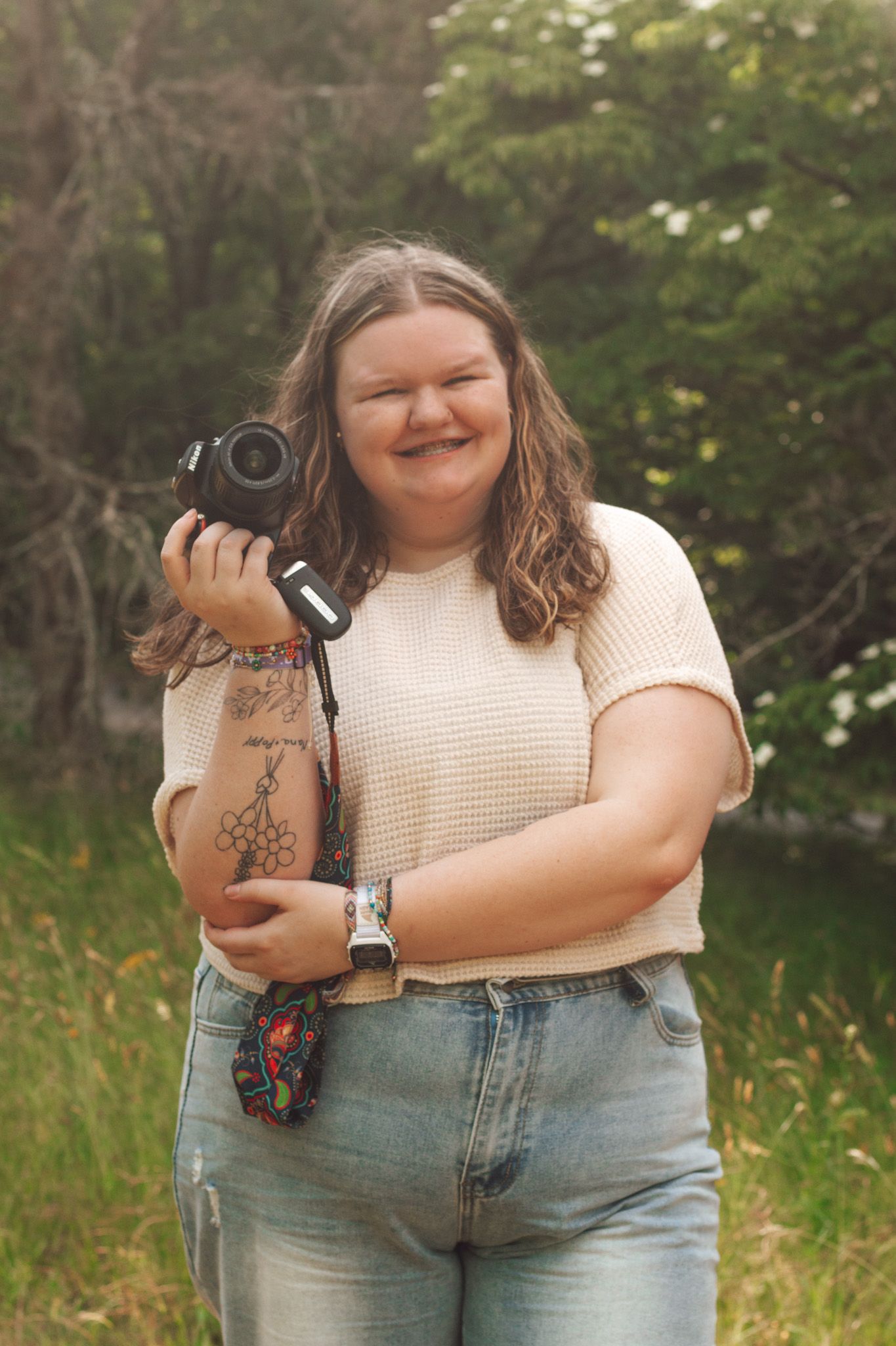 Photographer in casual attire practicing different camera poses outdoors in a grassy field.