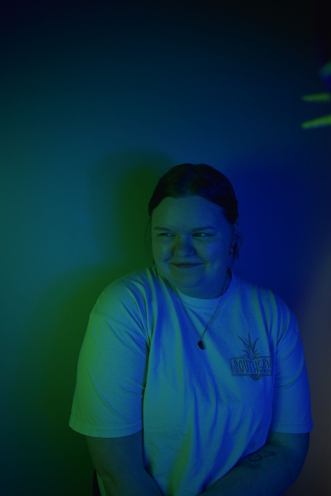 Person wearing white t-shirt illuminated by dramatic blue and green lighting.