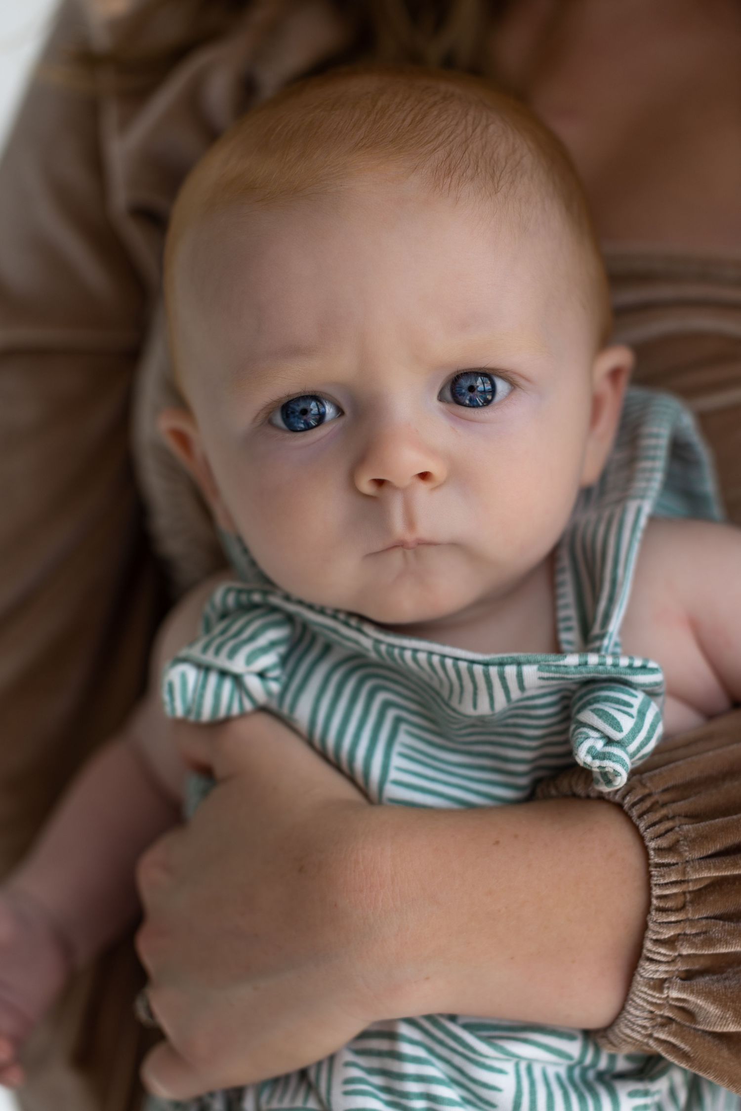 Baby wearing a striped outfit looks directly at camera with bright blue eyes.