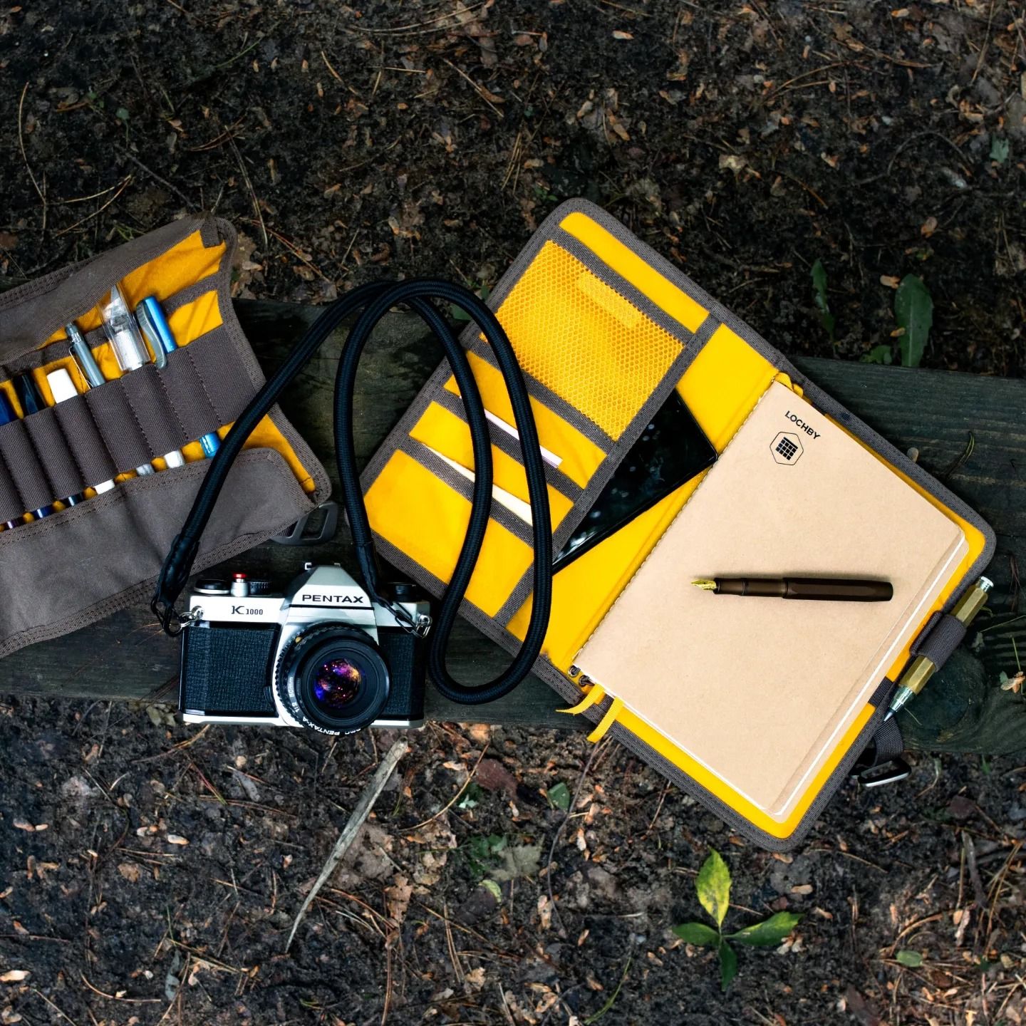 Flatlay of vintage camera, yellow safety vest, and writing materials on dark ground.