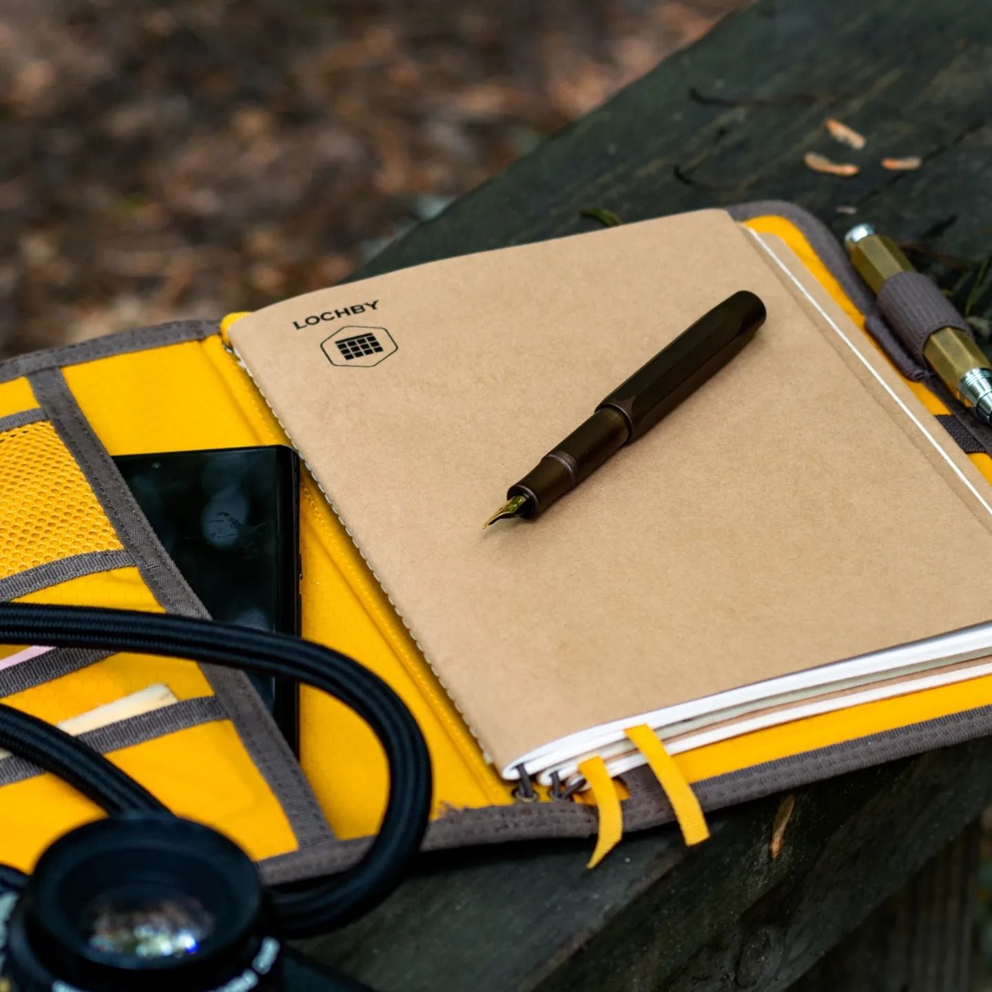 Yellow notebook with black pen resting on wooden surface outdoors.